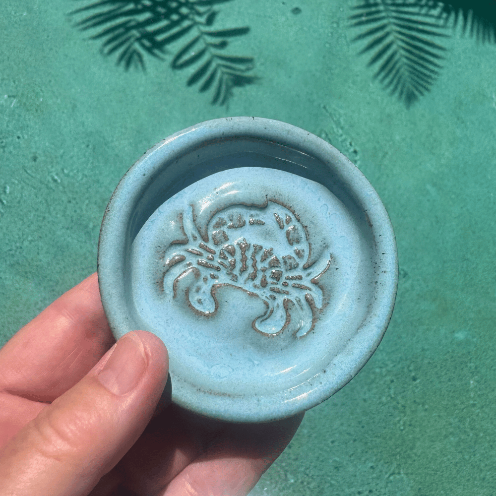 Ceramic trinket dish with crab design held by a hand against a teal background